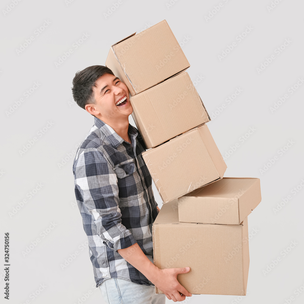 Asian man with moving boxes on light background