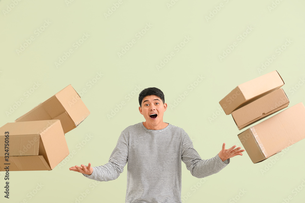 Asian man with moving boxes on color background