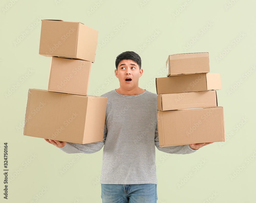 Asian man with moving boxes on color background