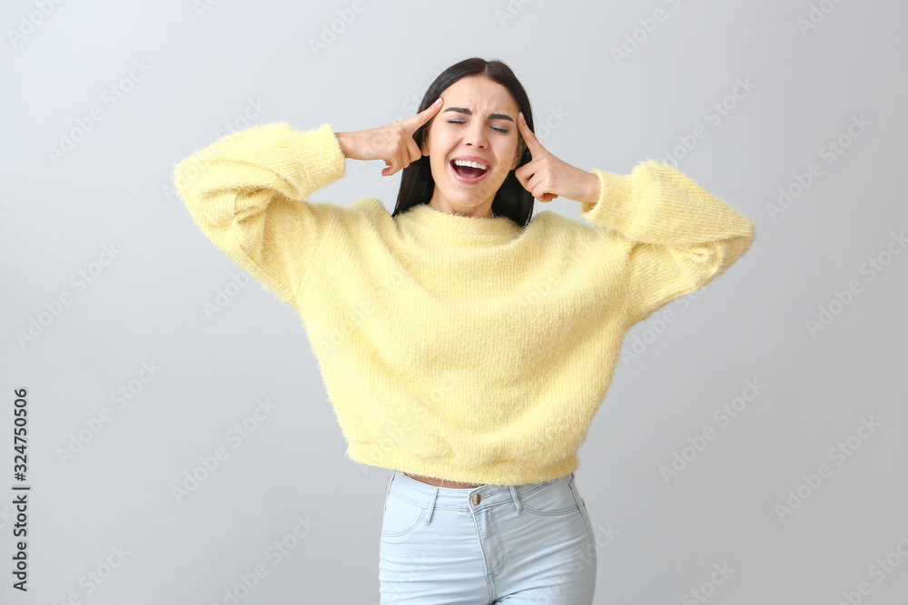 Emotional young woman in warm sweater on light background