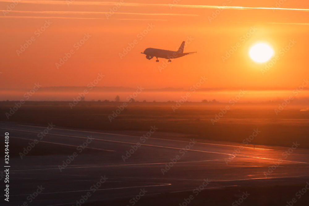 The photo shows a plane landing at dawn or sunset. The crimson rays of the sun nicely illuminate the