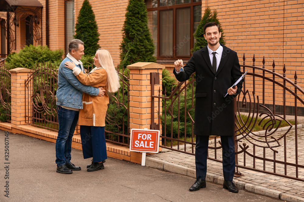 Male real estate agent with key and mature couple near house for sale outdoors