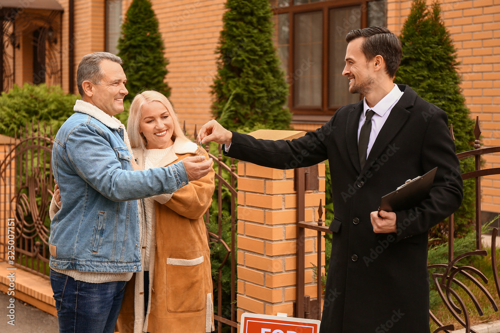 Male real estate agent giving a key from new house to mature couple outdoors