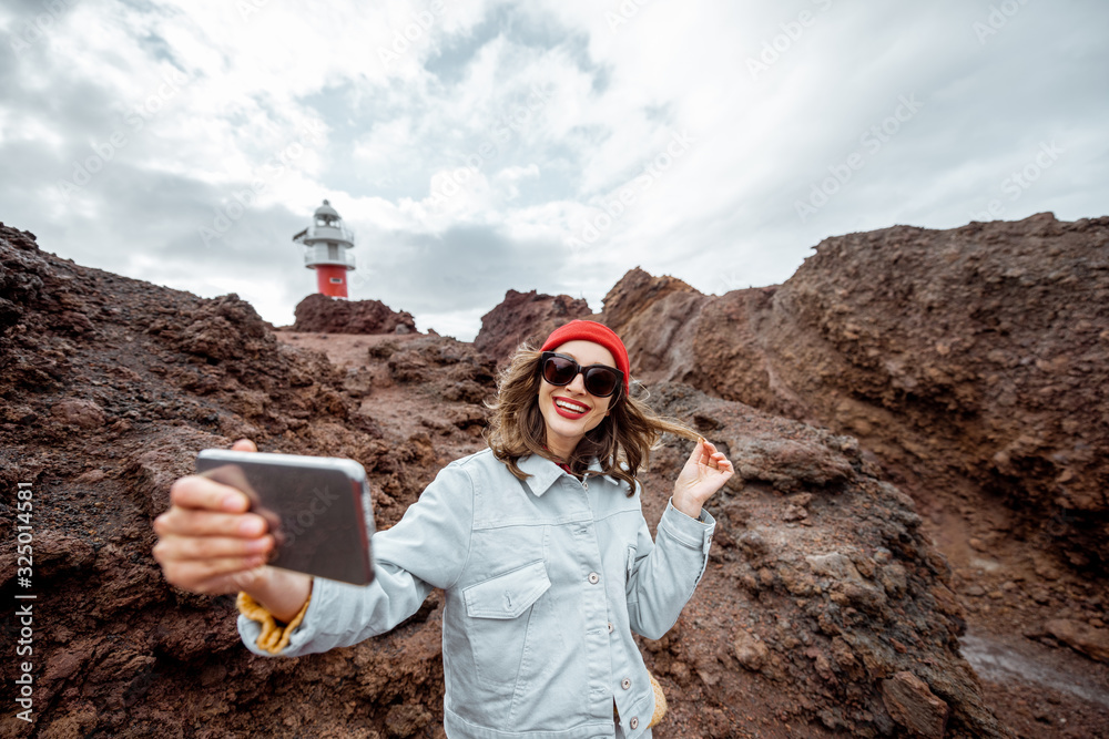 Carefree stylish woman enjoying trip on a rocky landscapes, making selfie photo near a Teno lighthou