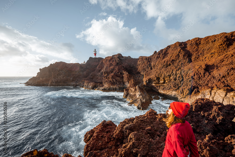 Woman enjoying great views on the rocky ocean coast and a lighthouse on the background, traveling on