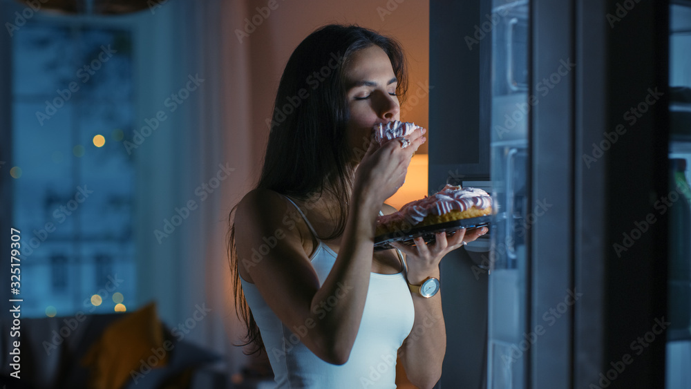 In the Kitchen in the Evening Hungry Beautiful Young Woman Bites a Piece of a Delicious Creamy Cake.