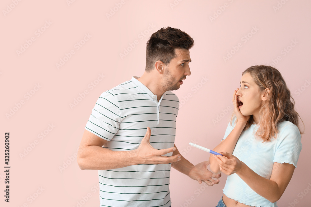 Emotional young couple with pregnancy test on color background