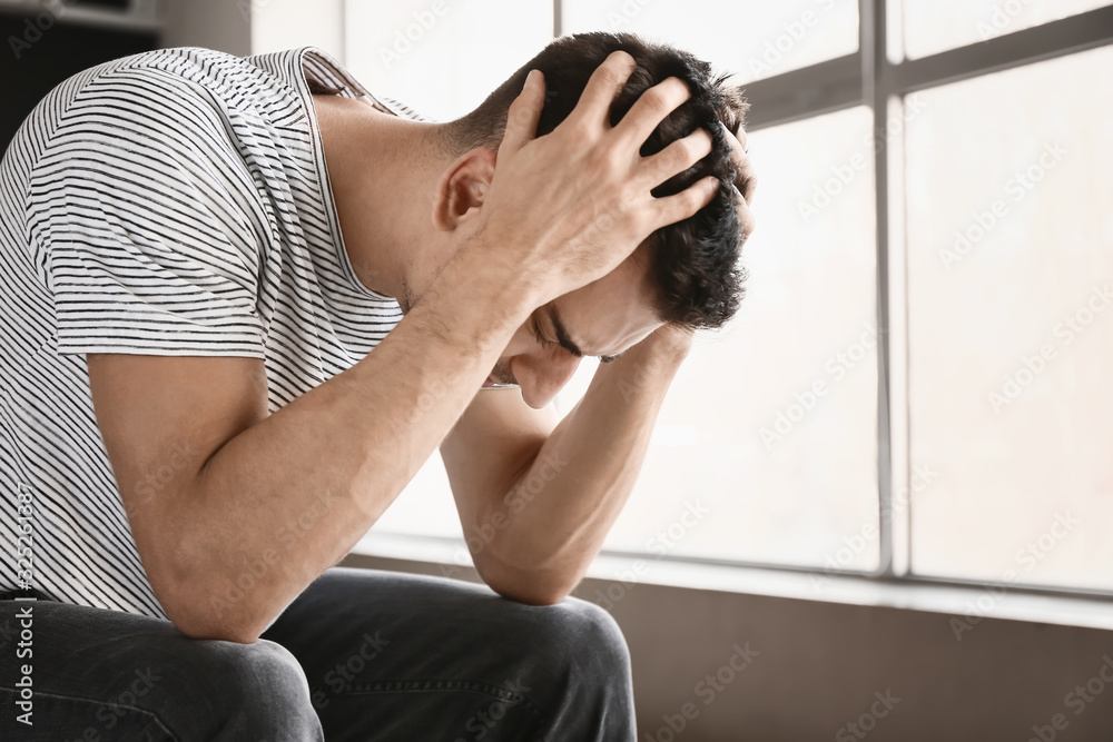 Depressed young man near window