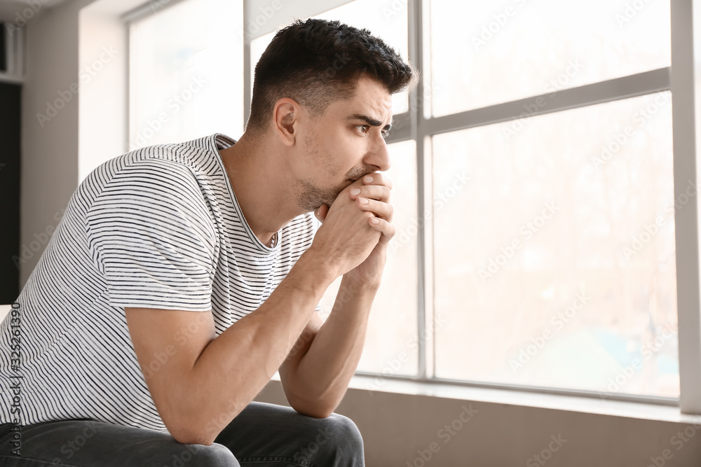 Depressed young man near window