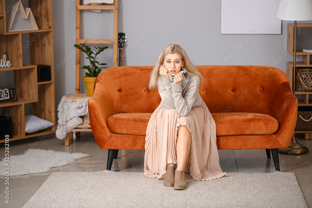 Beautiful young woman in warm sweater sitting on sofa at home