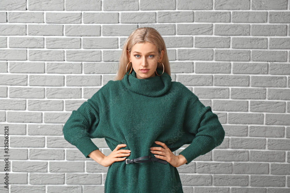 Beautiful young woman in warm sweater on brick background