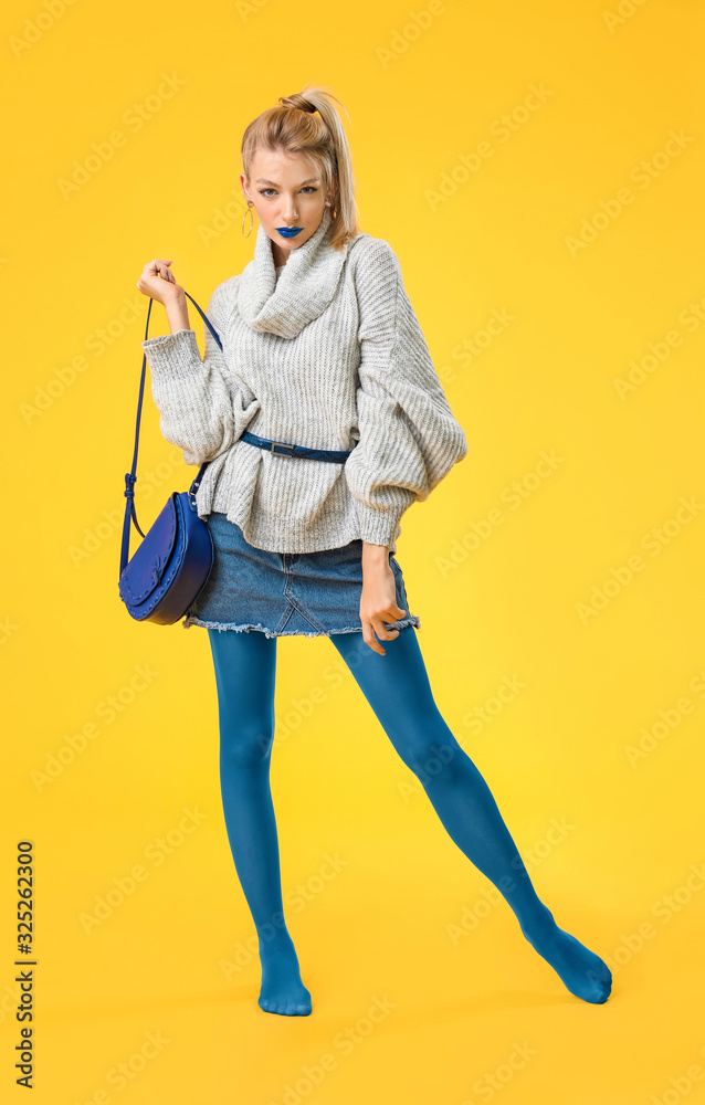 Young woman with creative makeup and in warm sweater on color background