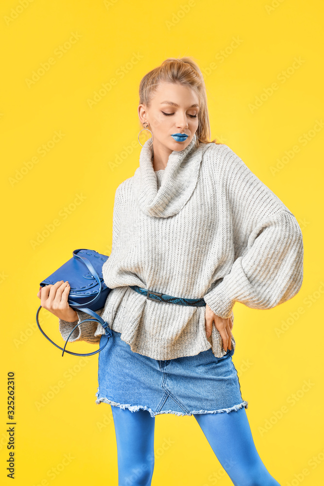 Young woman with creative makeup and in warm sweater on color background