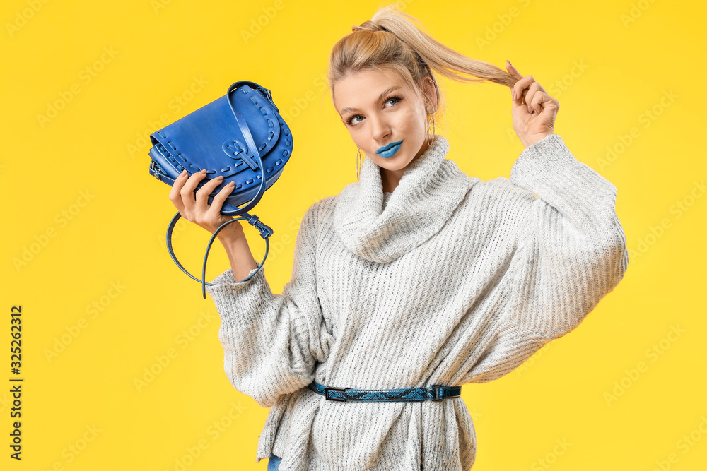 Young woman with creative makeup and in warm sweater on color background