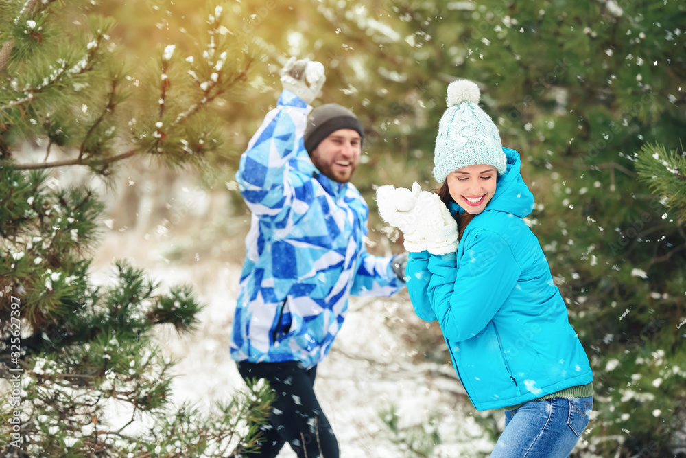 Happy young couple playing snowballs in park on winter day