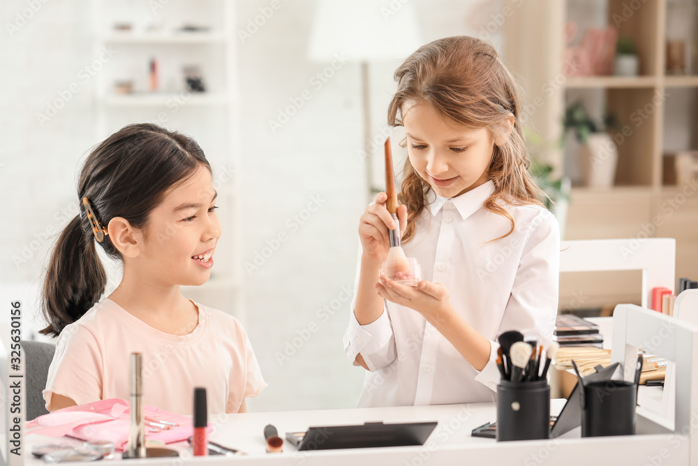 Cute little girl applying makeup on her friends face at home