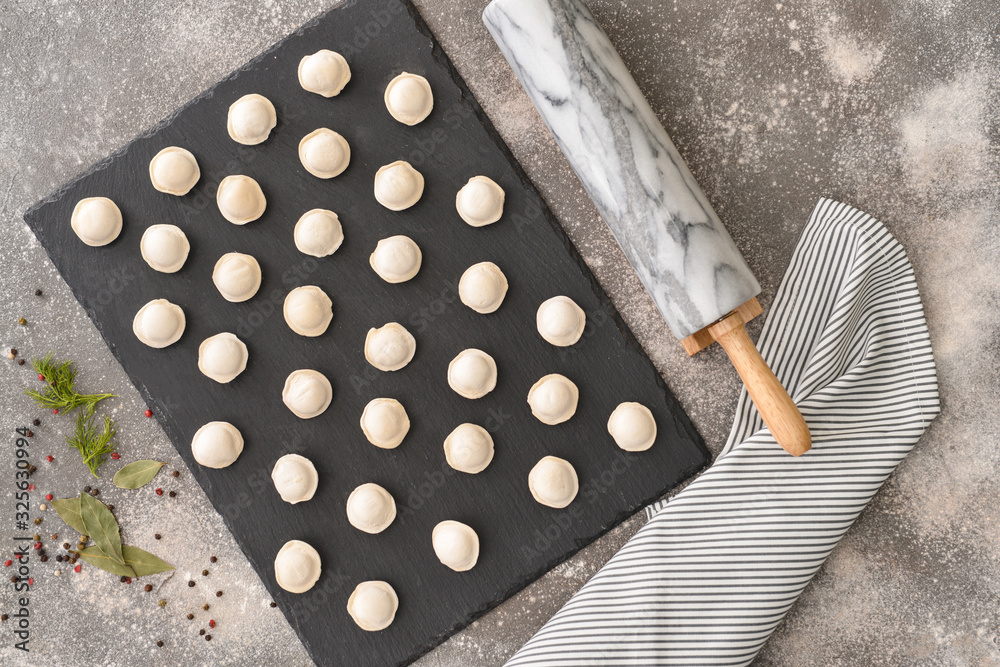 Raw fresh dumplings with rolling pin on grey background