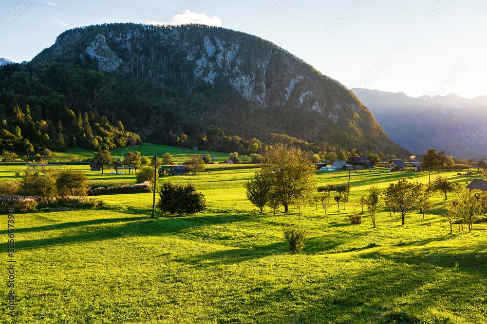 Mountain at sunset. Sunlight illuminates houses in the field and trees. Valley in the mountains and 