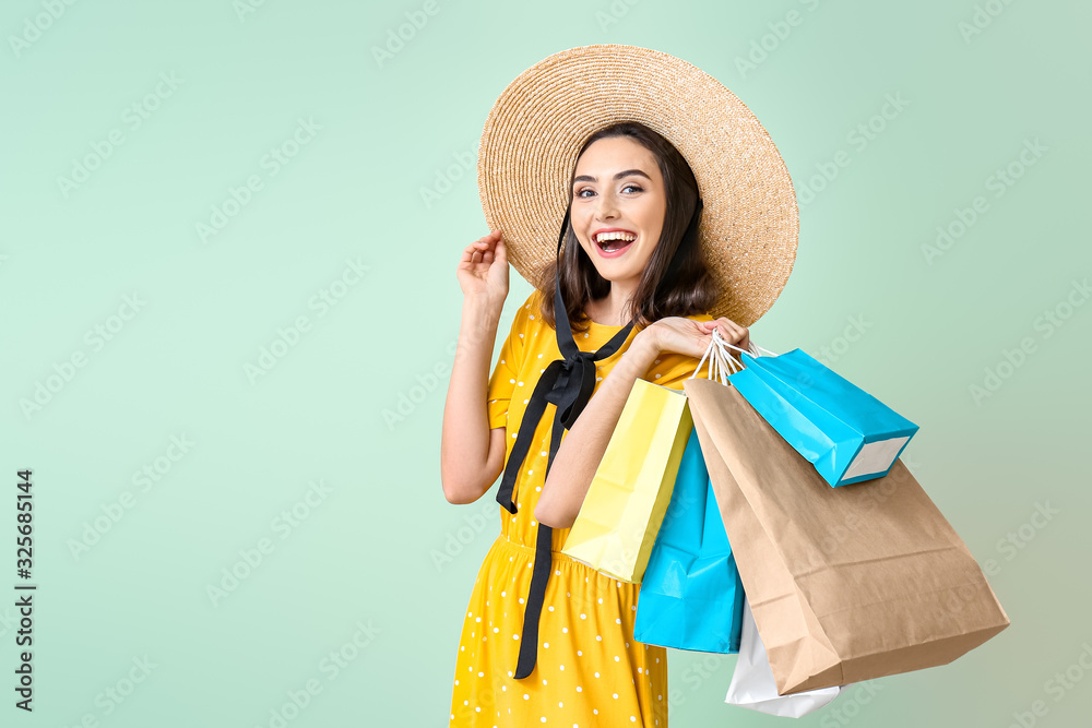 Beautiful young woman with shopping bags on color background