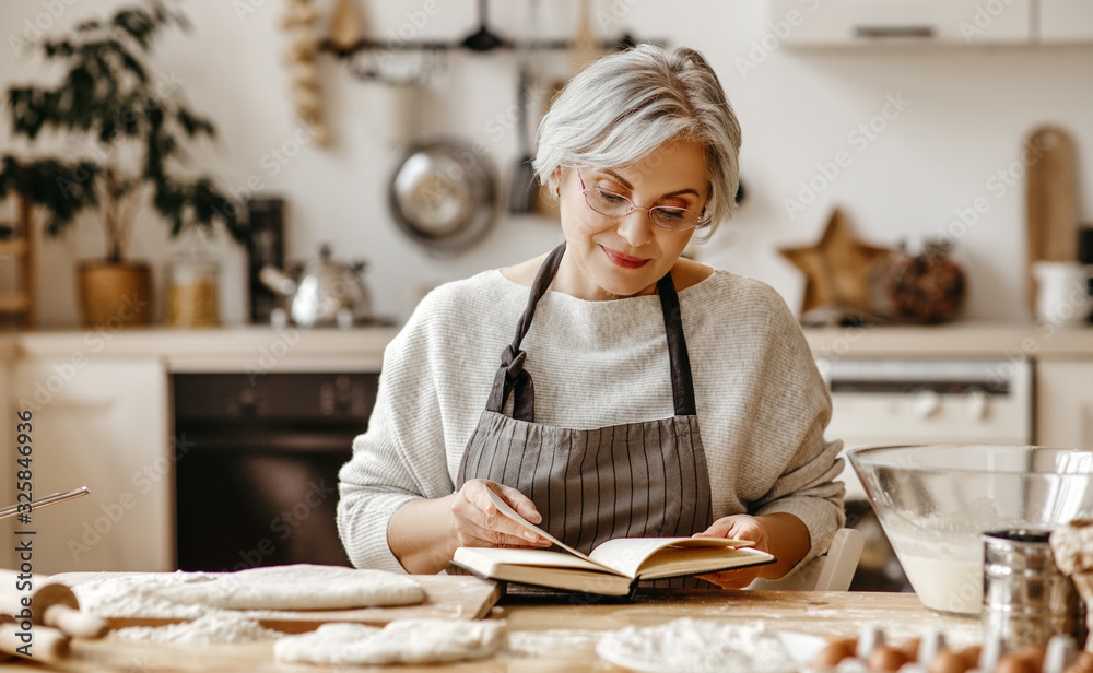 happy old woman Granny cooks in kitchen kneads dough, bakes cookies.