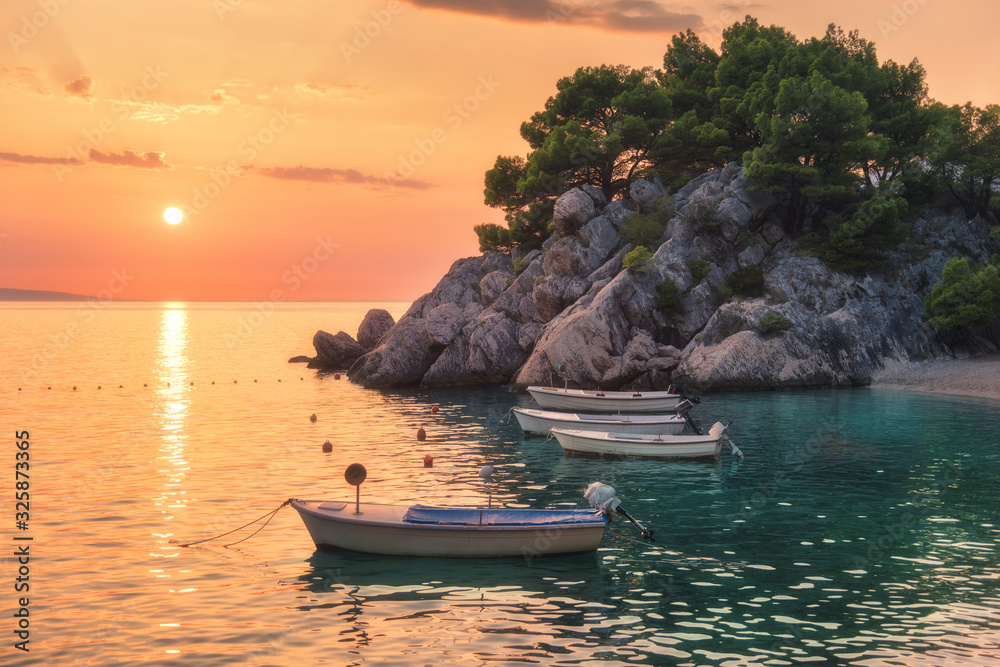 Beautiful boats on the sea and green trees growing out of the rock at sunset in summer in Croatia. C