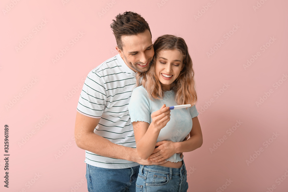 Happy young couple with pregnancy test on color background