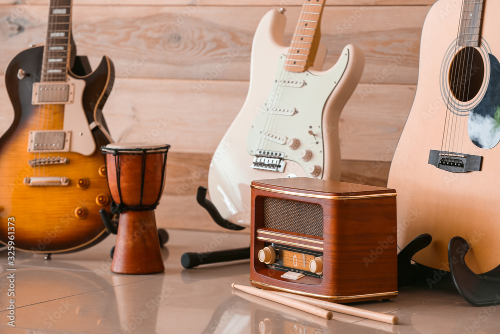 Modern guitars, drum and radio receiver near wooden wall