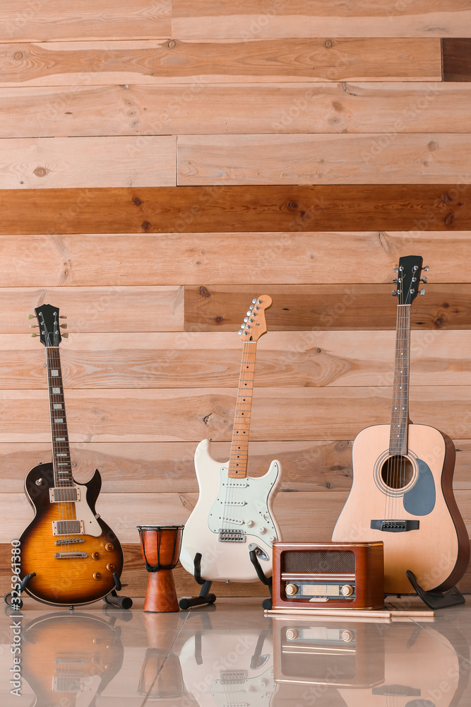 Modern guitars, drum and radio receiver near wooden wall