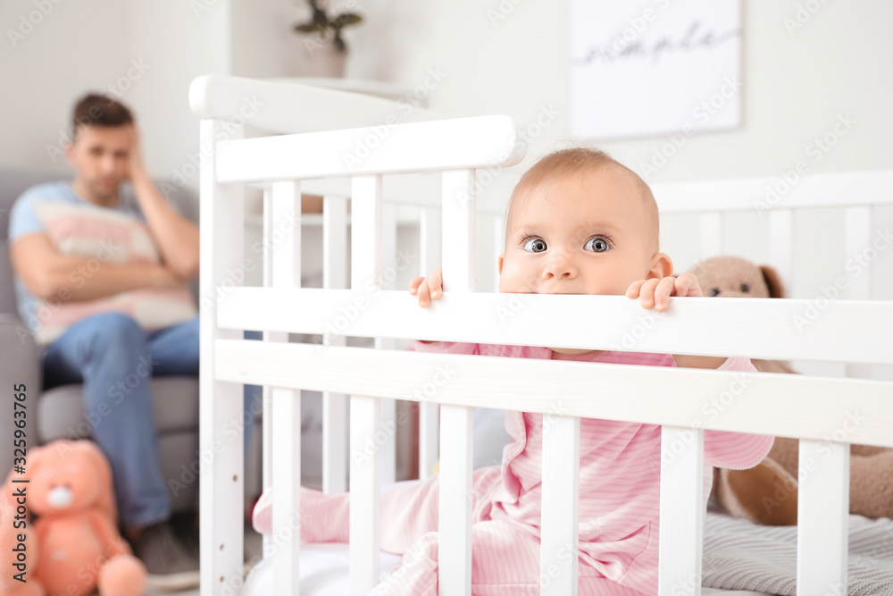 Cute baby in bed and young father suffering from postnatal depression at home