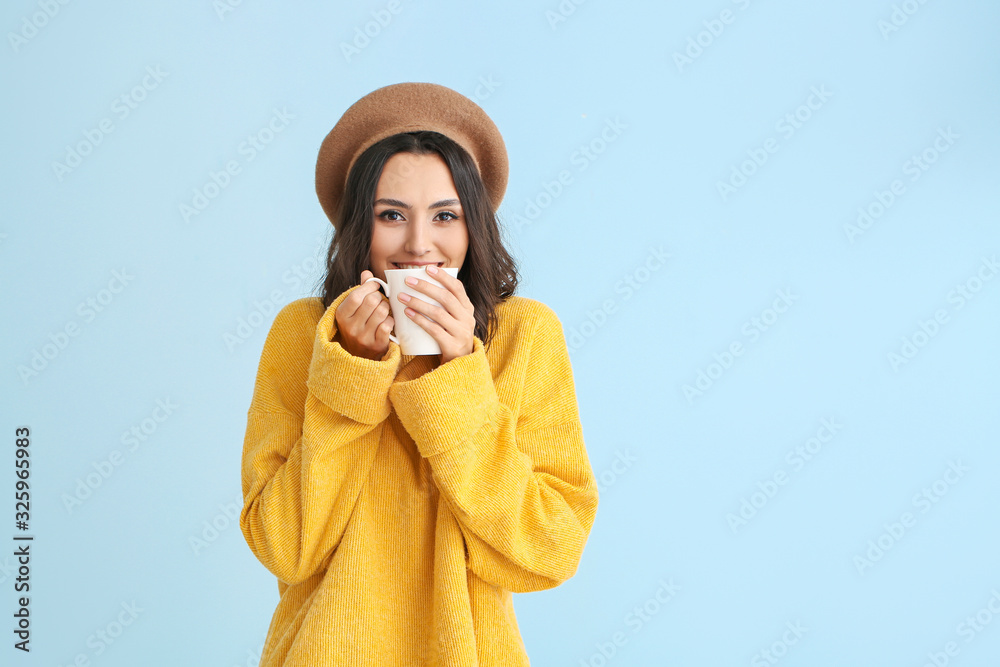 穿着保暖毛衣的漂亮年轻女子在彩色背景下喝茶