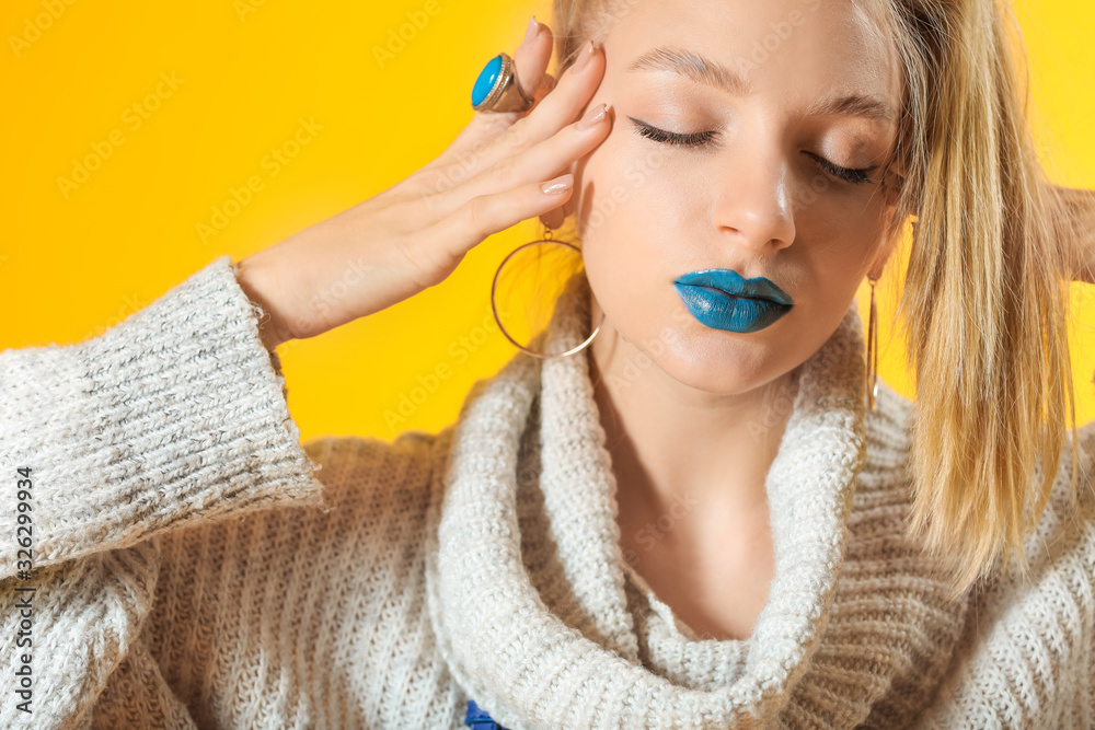 Young woman with creative makeup and in warm sweater on color background