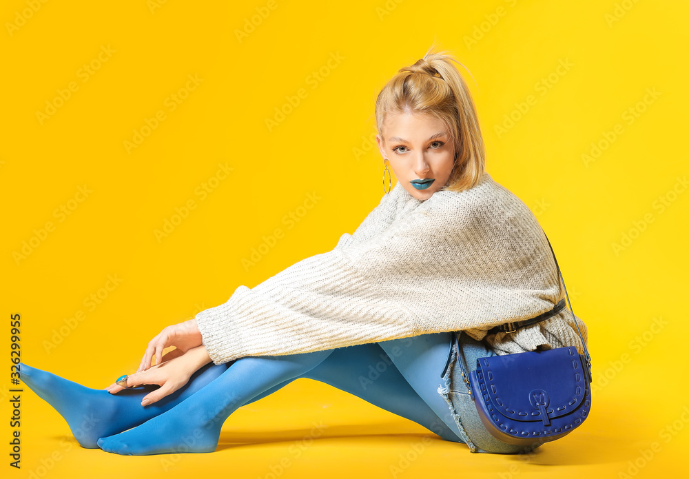 Young woman with creative makeup and in warm sweater on color background