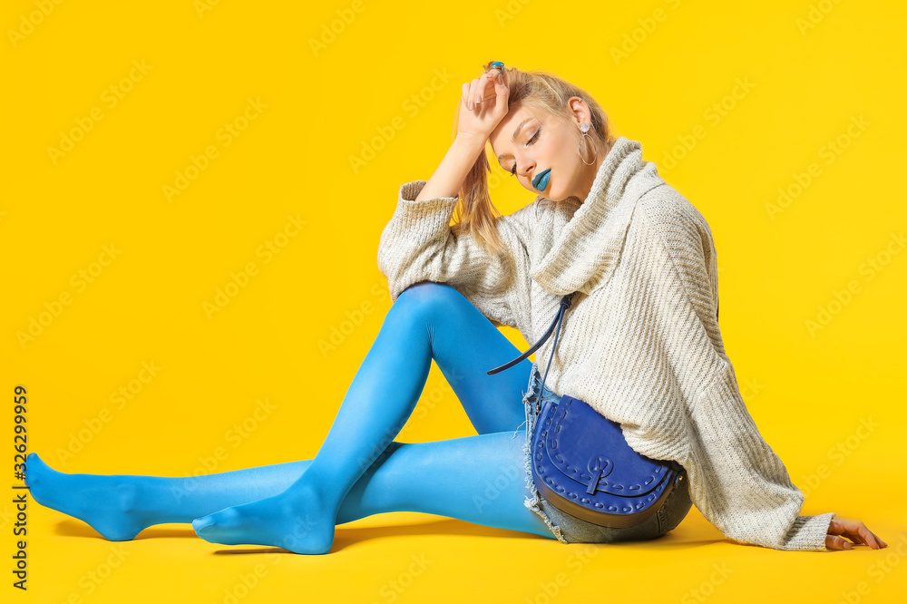 Young woman with creative makeup and in warm sweater on color background