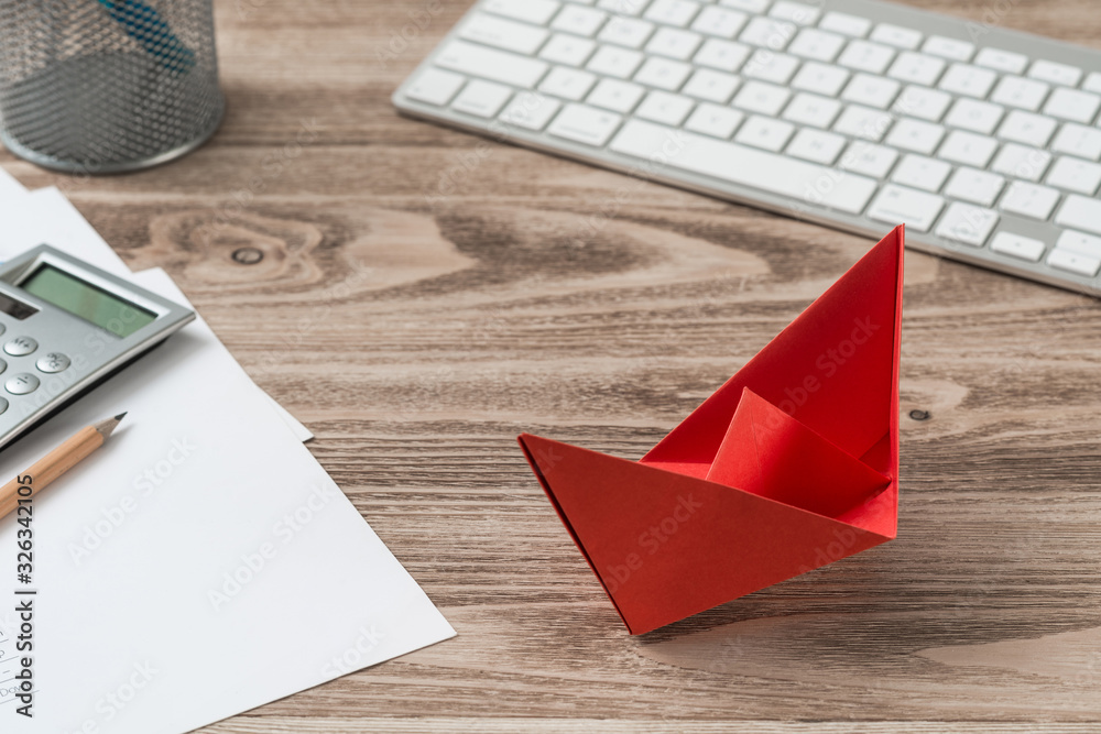 Top view office workspace with red paper ship