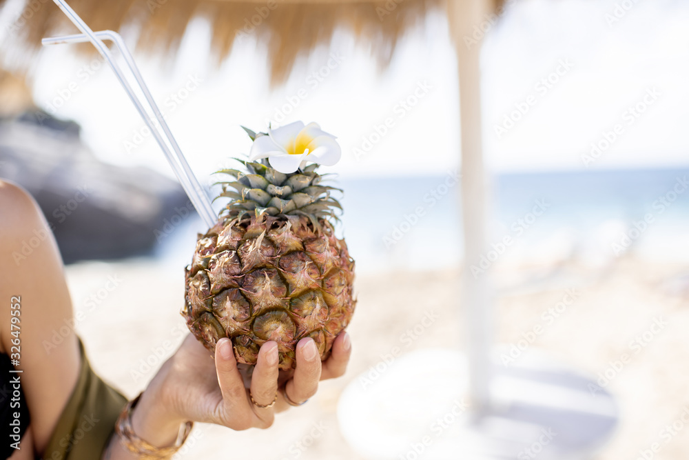 一名女子在海滩度假胜地拿着异国情调的夏季鸡尾酒，特写菠萝上的花朵和dr