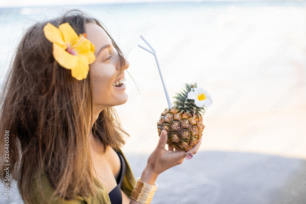 Portrait of a beautiful smiling woman with hair flower and exotic cocktail at the beach on a sunny d