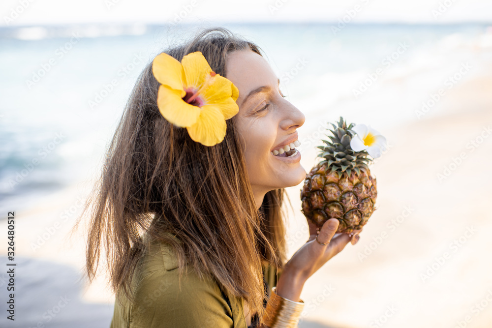 Portrait of a beautiful smiling woman with hair flower and pineapple fruit at the beach on a sunny d