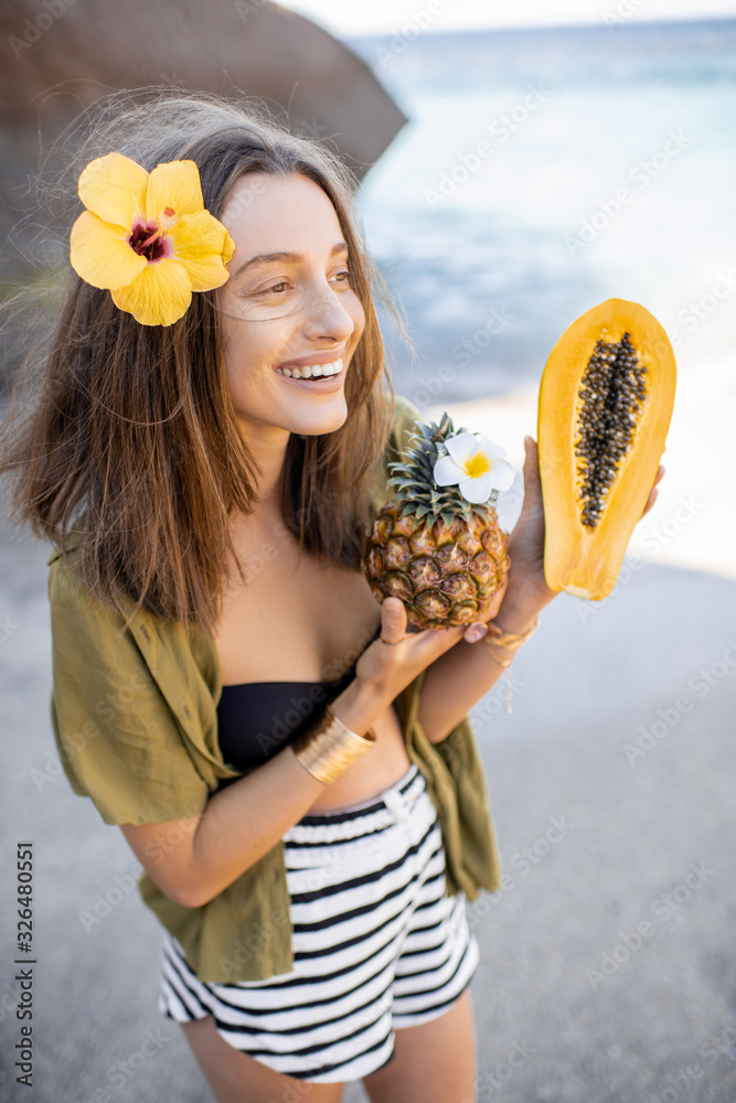 Portrait of a beautiful smiling woman with hair flower and exotic fruits at the beach on a sunny day