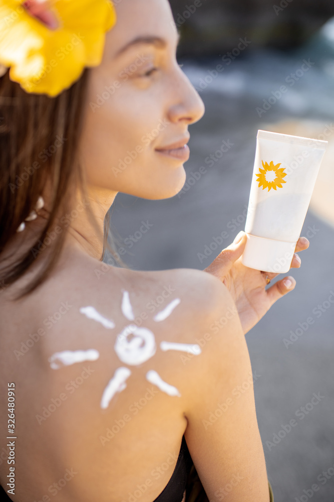 Portrait of a beautiful young woman with sun shape on her shoulder holding tube with sunscreen lotio