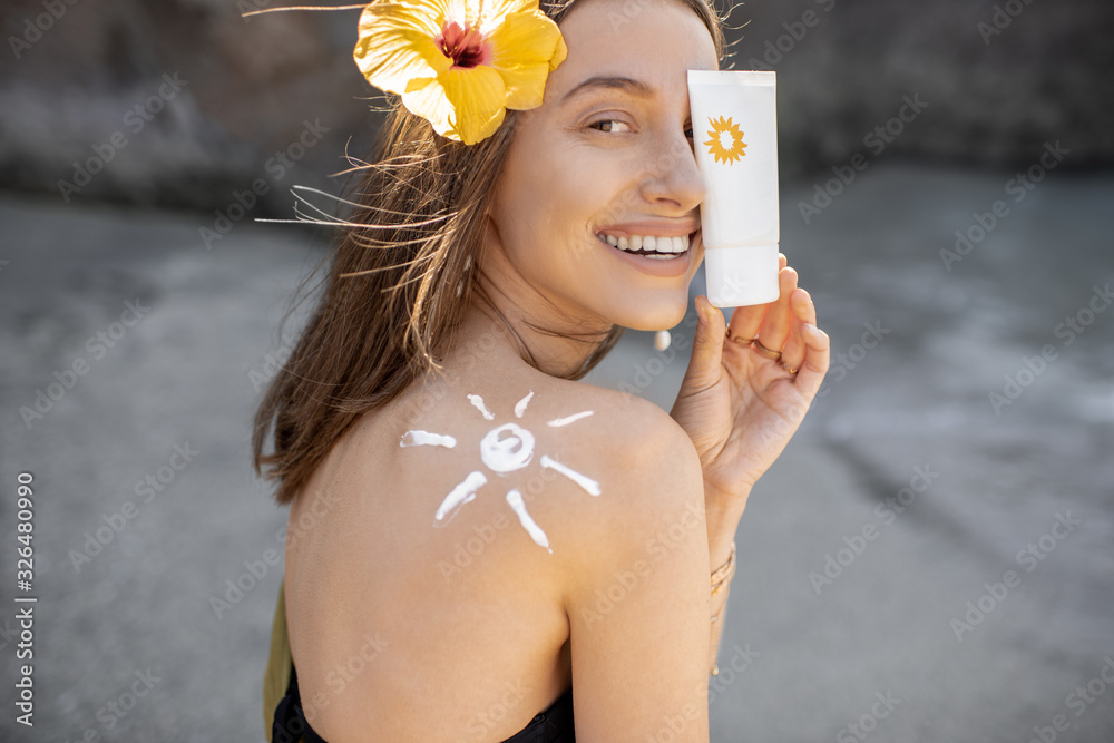 Portrait of a beautiful young woman with sun shape on her shoulder holding tube with sunscreen lotio