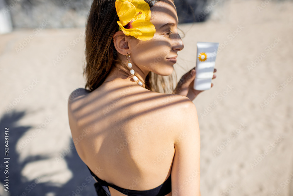 Portrait of a cute summer girl with sunscreen lotion and hair flower shaded with palm leaves on the 