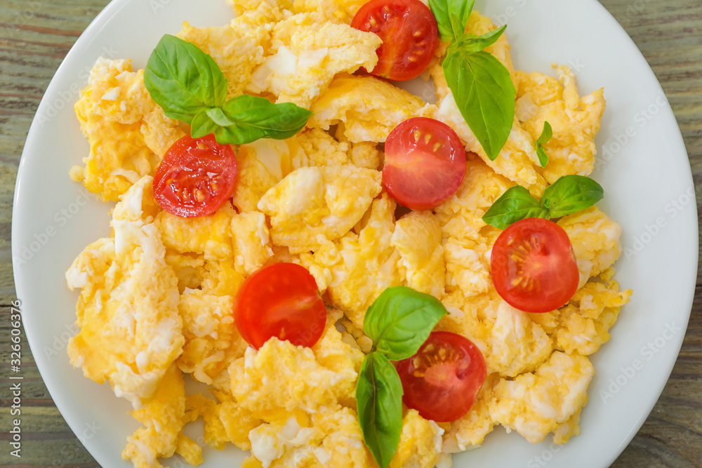 Tasty scrambled eggs with tomatoes and basil on plate