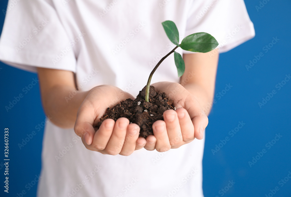 Little boy holding soil and plant on color background, closeup. Earth Day celebration