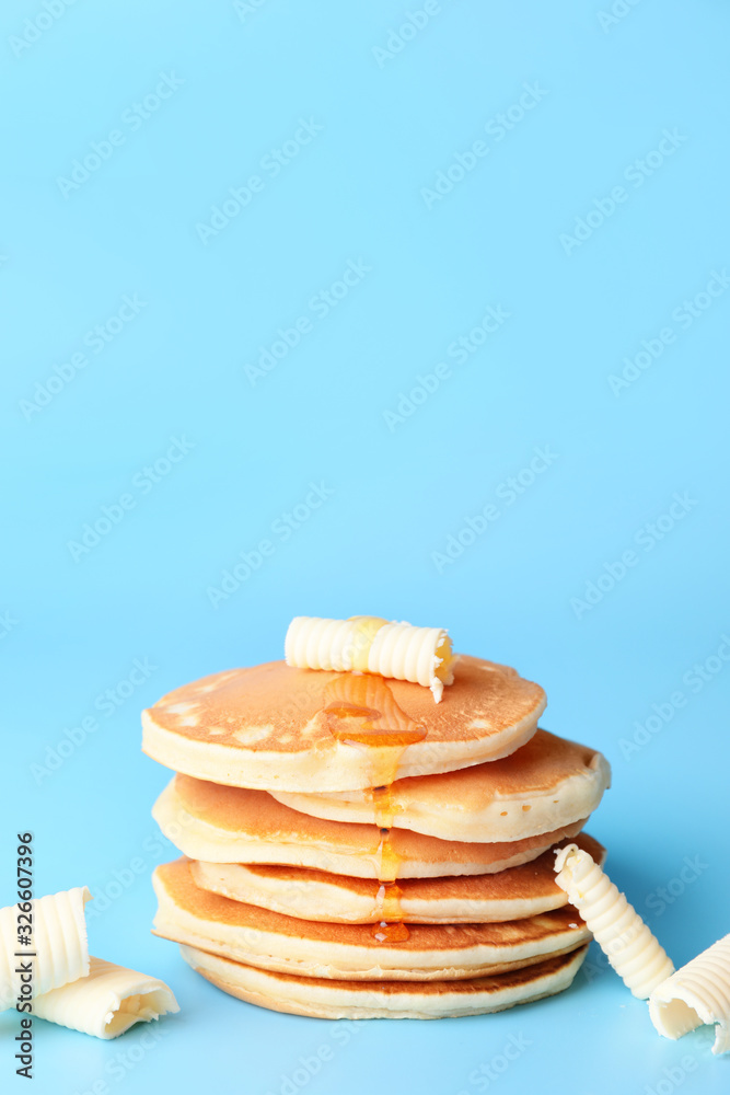 Tasty pancakes with honey and butter on color background