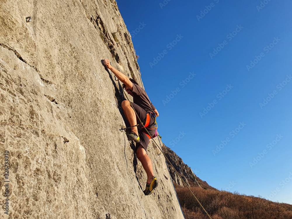 Young man fearlessly climbs up a rocky cliff on perfect day for rock climbing