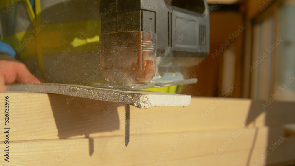 MACRO, DOF: Unrecognizable builder cuts a plasterboard with a rusty jigsaw.