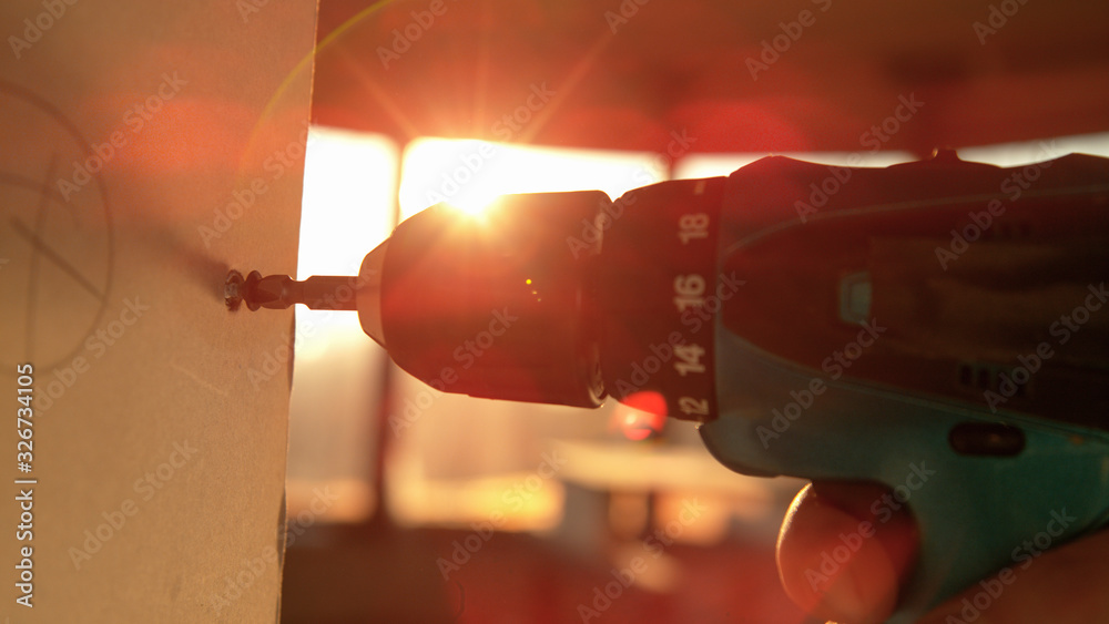 MACRO: Unrecognizable contractor uses a power drill to unscrew a bolt at sunrise