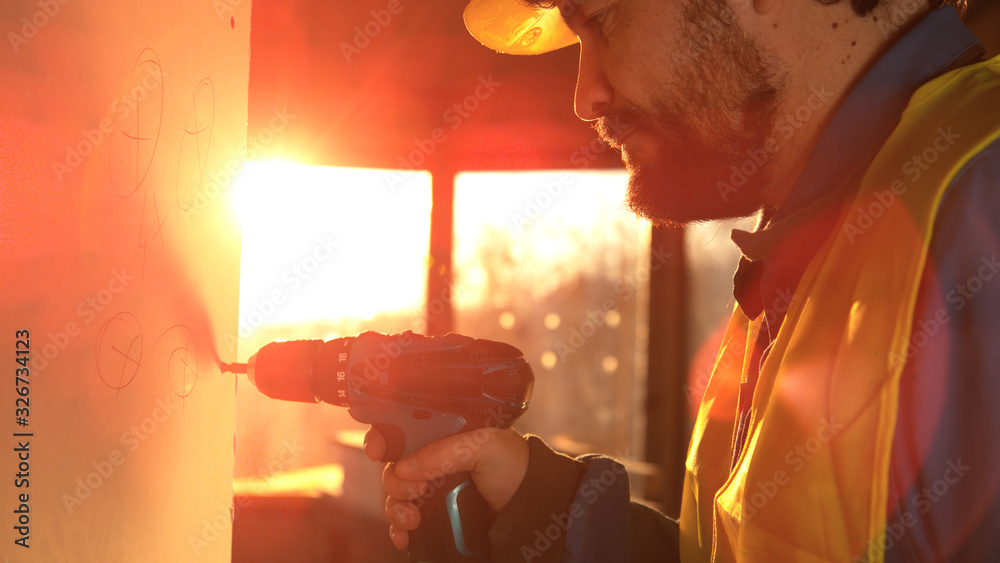 CLOSE UP LENS FLARE: Caucasian builder unscrews a bolt stuck in a wall panel.