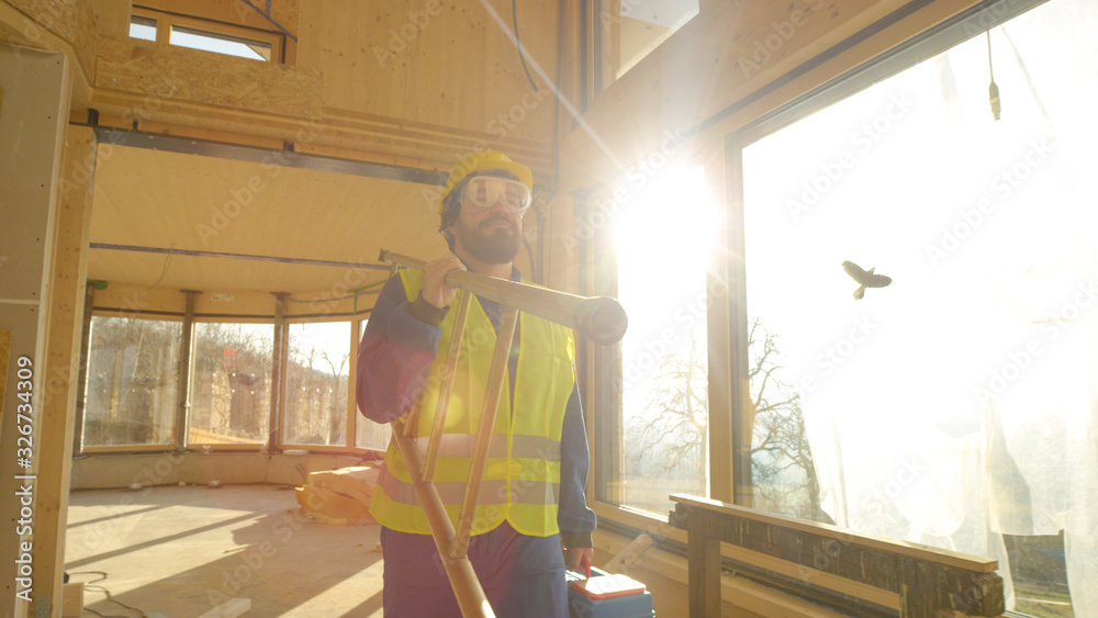 CLOSE UP Builder in blue coveralls leaves prefabricated house on a sunny evening