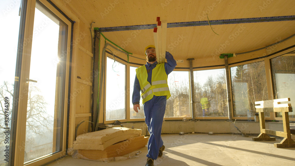 LOW ANGLE: Worker arrives to work carrying heavy wooden beams on his shoulder